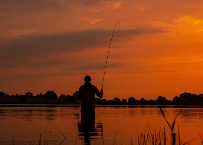 Silhouette Of Person Fishing In Lake At Sunset j43xf2