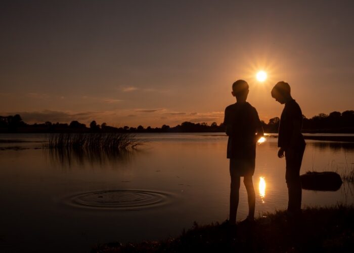 Silhouettes of two boys at lakeside sunset a52u0w