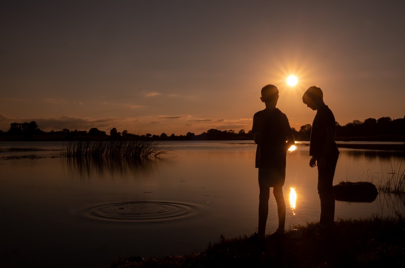 Silhouettes of two boys at lakeside sunset a52u0w