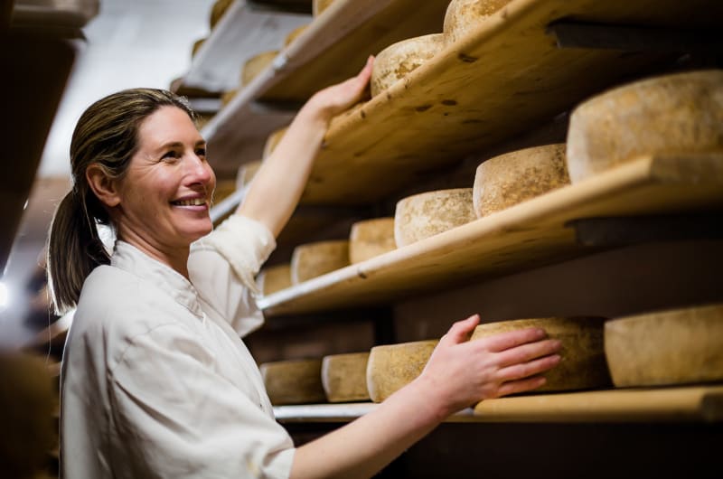 Smiling woman inspecting cheese wheels on wooden shelves