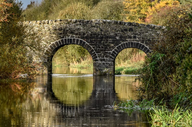 Stone Arched Bridge Reflecting In River During Autumn