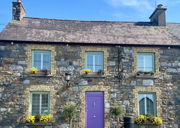 Stone House With Purple Door And Yellow Flowers ks9z9o
