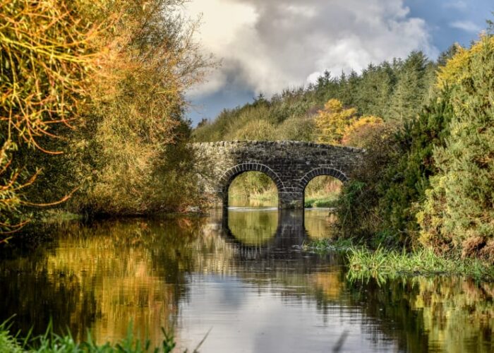Stone arch bridge reflecting in calm autumn river bxj7q9