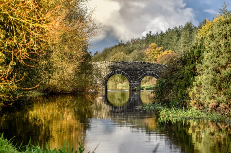 Stone arch bridge reflecting in calm autumn river bxj7q9