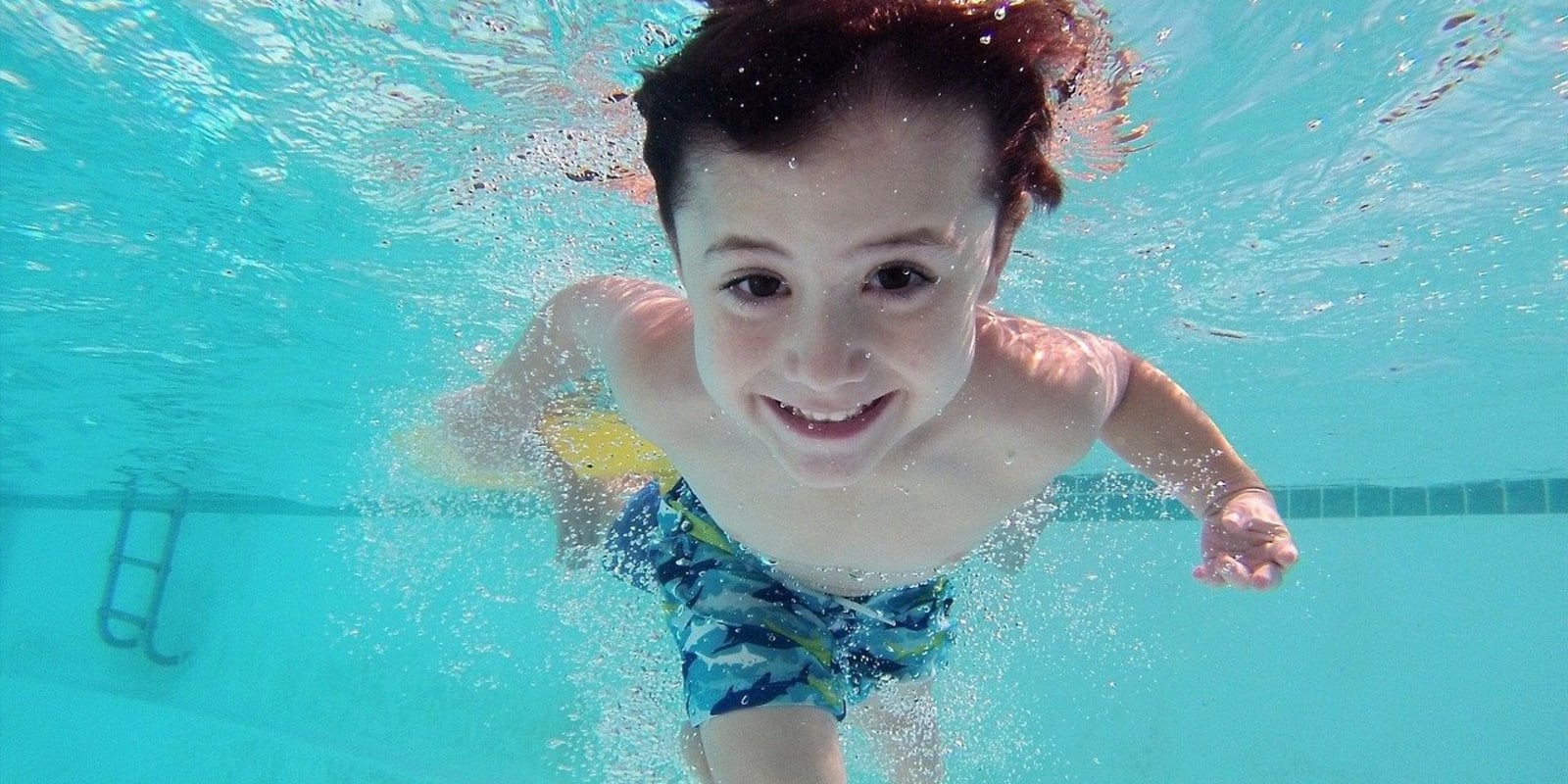Swiming Pools Header Image Smiling boy swimming underwater in a pool