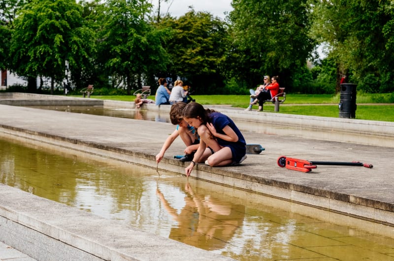 Two Children Playing With Sticks By Park Pool apfd4t