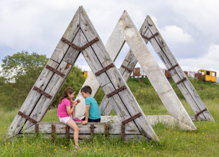 Two children sitting inside large triangular wooden structures