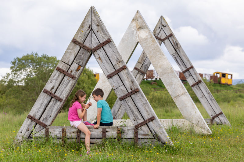 Two children sitting inside large triangular wooden structures