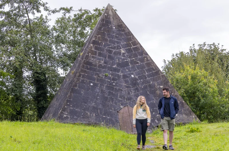Two people walking near large stone pyramid structure lq6wmx