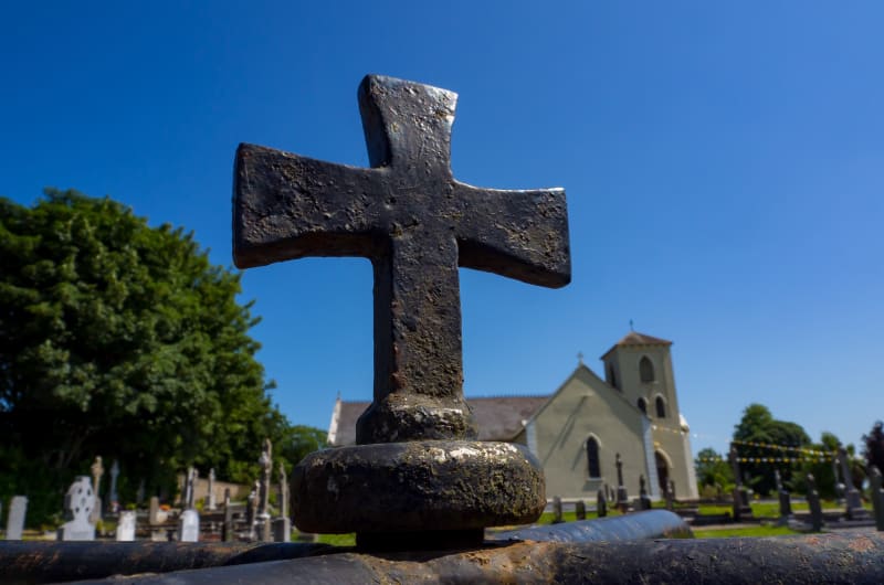 Weathered black cross in graveyard with church background fvn6bq
