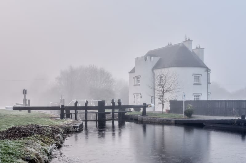 White Lock House By Frozen Canal In Fog