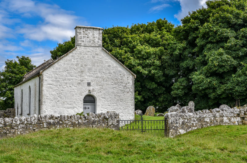 White Stone Chapel Behind Stone Wall And Gate