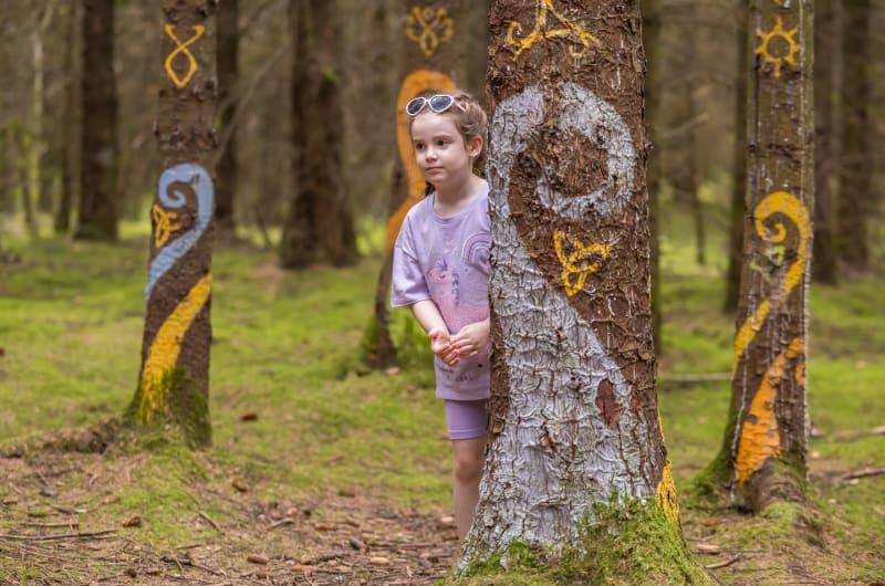 Young Girl Standing Beside Painted Trees In Forest e3exgy