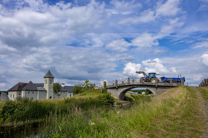 Blue Tractor Crossing Stone Bridge Near Building pqwhpj