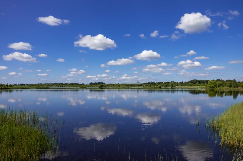 Clear blue sky with white clouds reflecting on lake wmxhnf