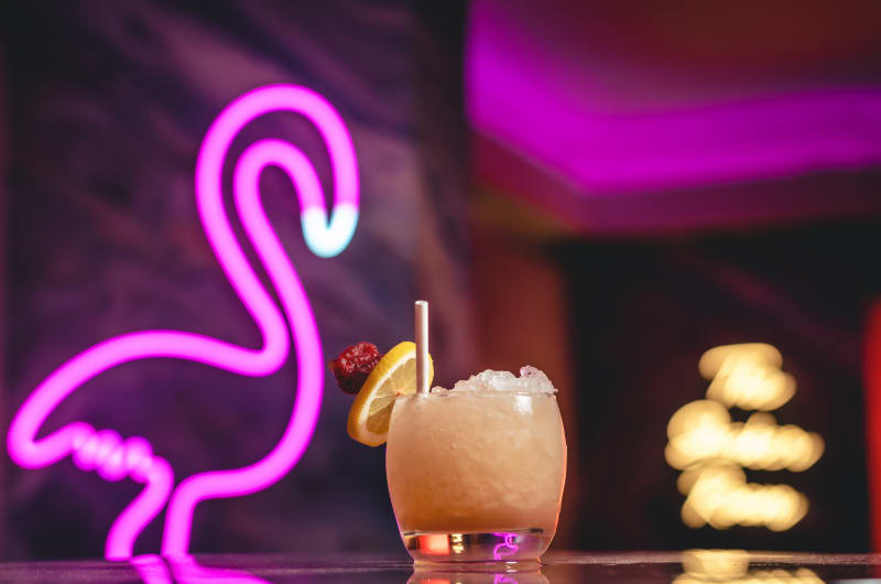 Cocktail with fruit garnish and neon flamingo background