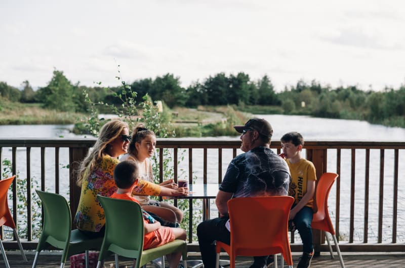 Family Sitting At An Outdoor Lakeside Table kfyclg