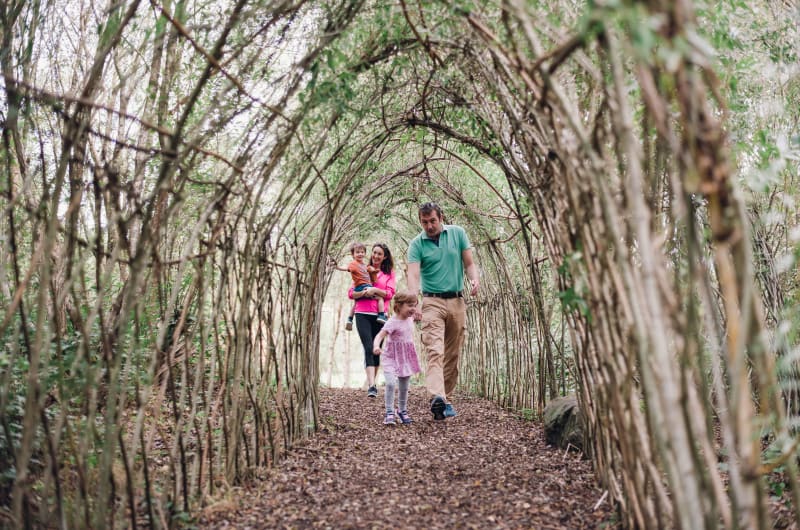 Family Walking Through A Natural Woven Branch Tunnel fhtddw