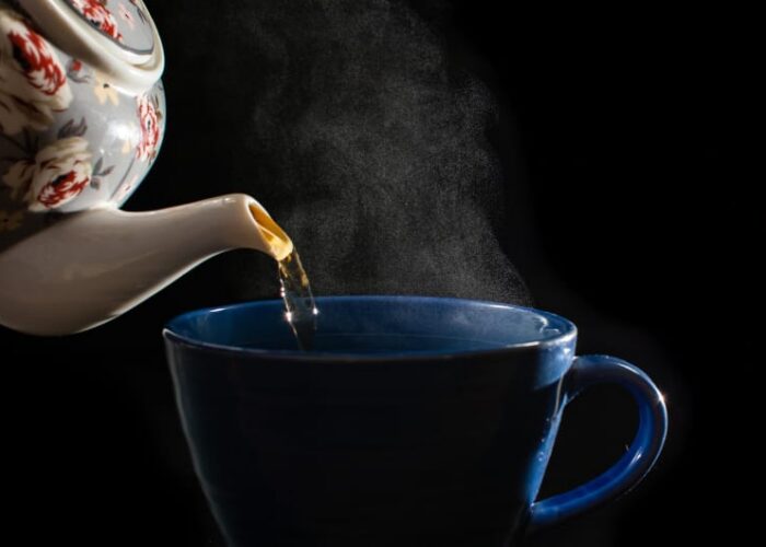 Teapot pouring steaming tea into blue mug