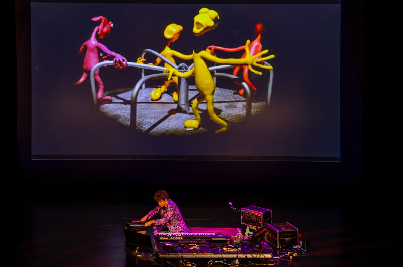 electronic musician on stage with screen in background