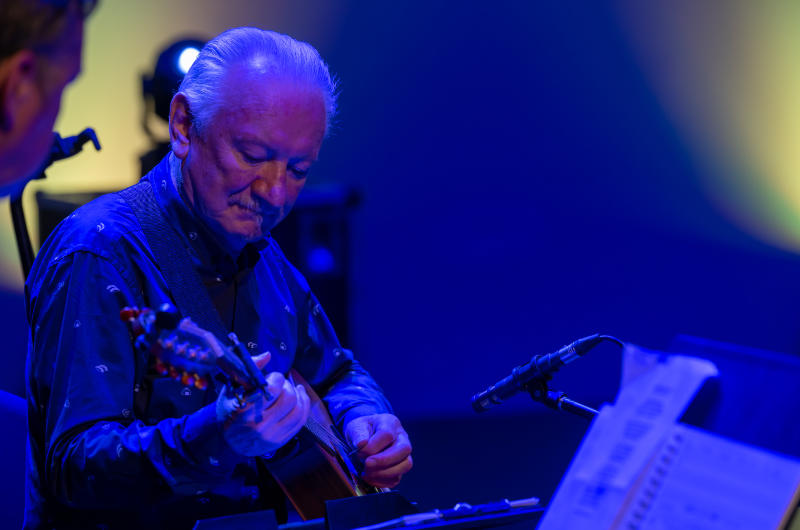 older man playing guitar on stage blue lighting
