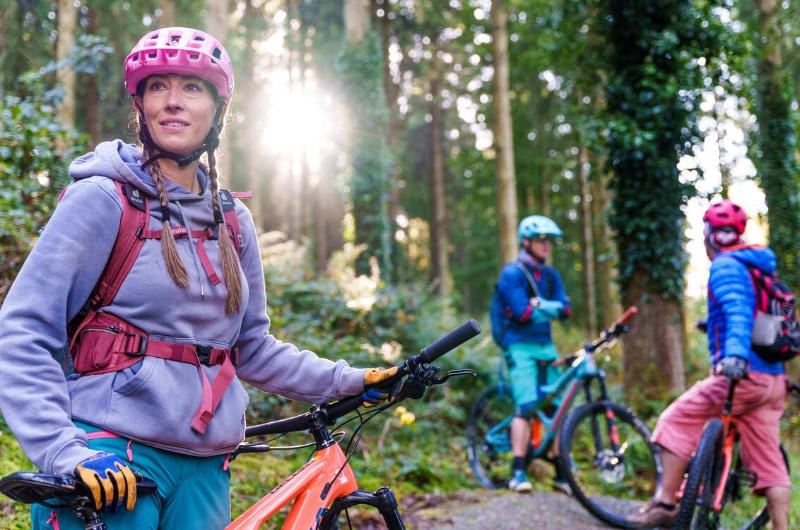 two people and woman in foreground with mountain bikes forest