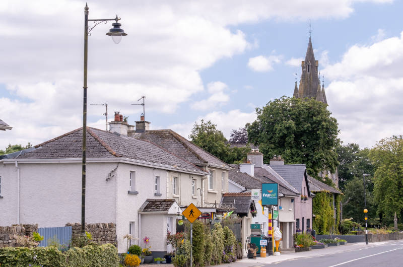 village street with church steeple showing through trees