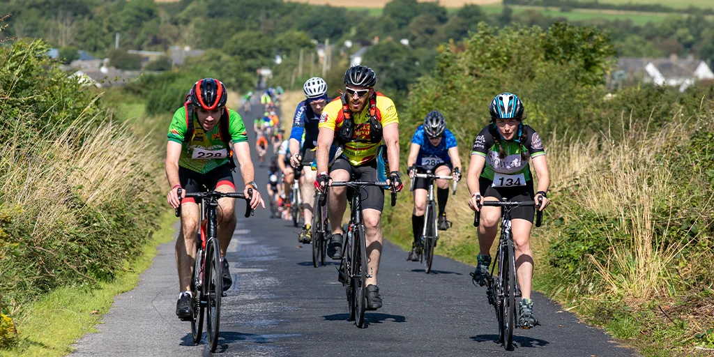 Cyclists wearing helmets and jerseys riding up a paved road during a countryside cycling event