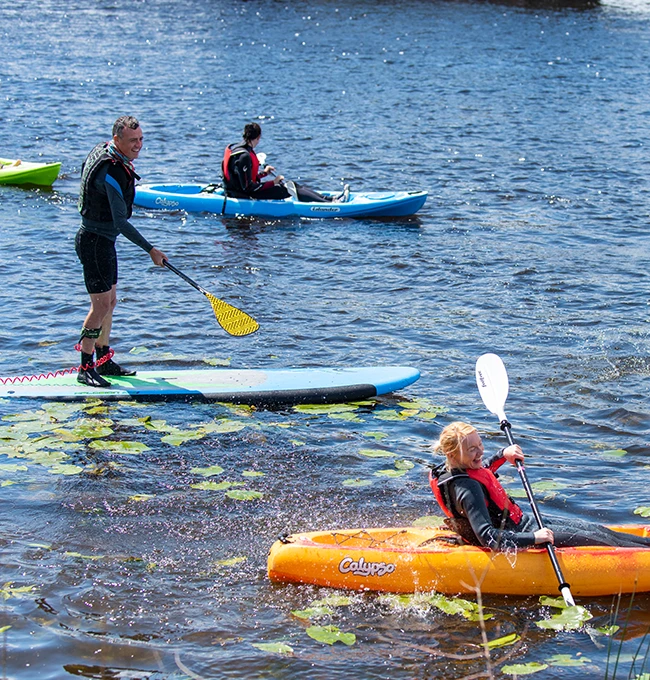 Man standing on SUP board and woman in kayaking in water laughing